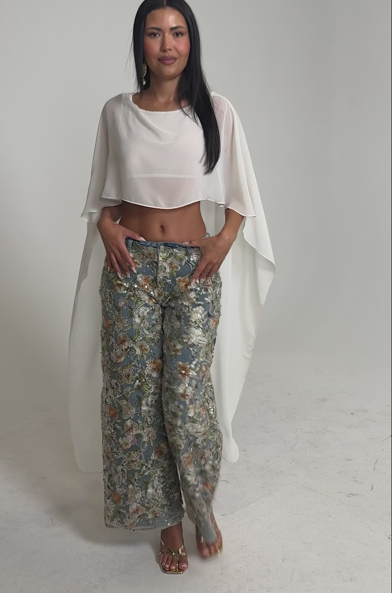 Video of woman modeling the IRIS RELAXED DENIM WITH FLORAL OVERLAY, featuring colorful embroidery and sequins, paired with gold open-toe heels
