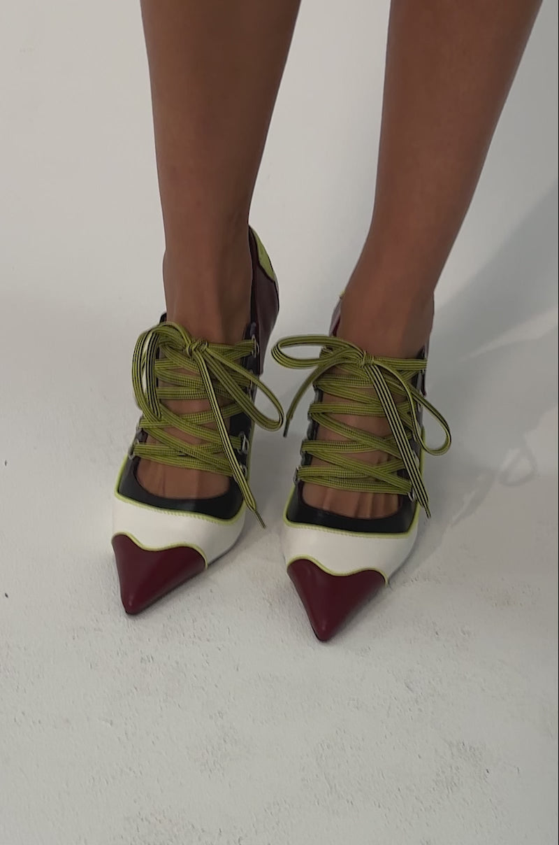 Video of woman modeling the AZALEA WANG BLITZ MULTI COLOR LACE UP STILETTO PUMP, featuring pointed toes, a colorblock heel in burgundy, black, white, and yellow-green accents with lace-up details. 