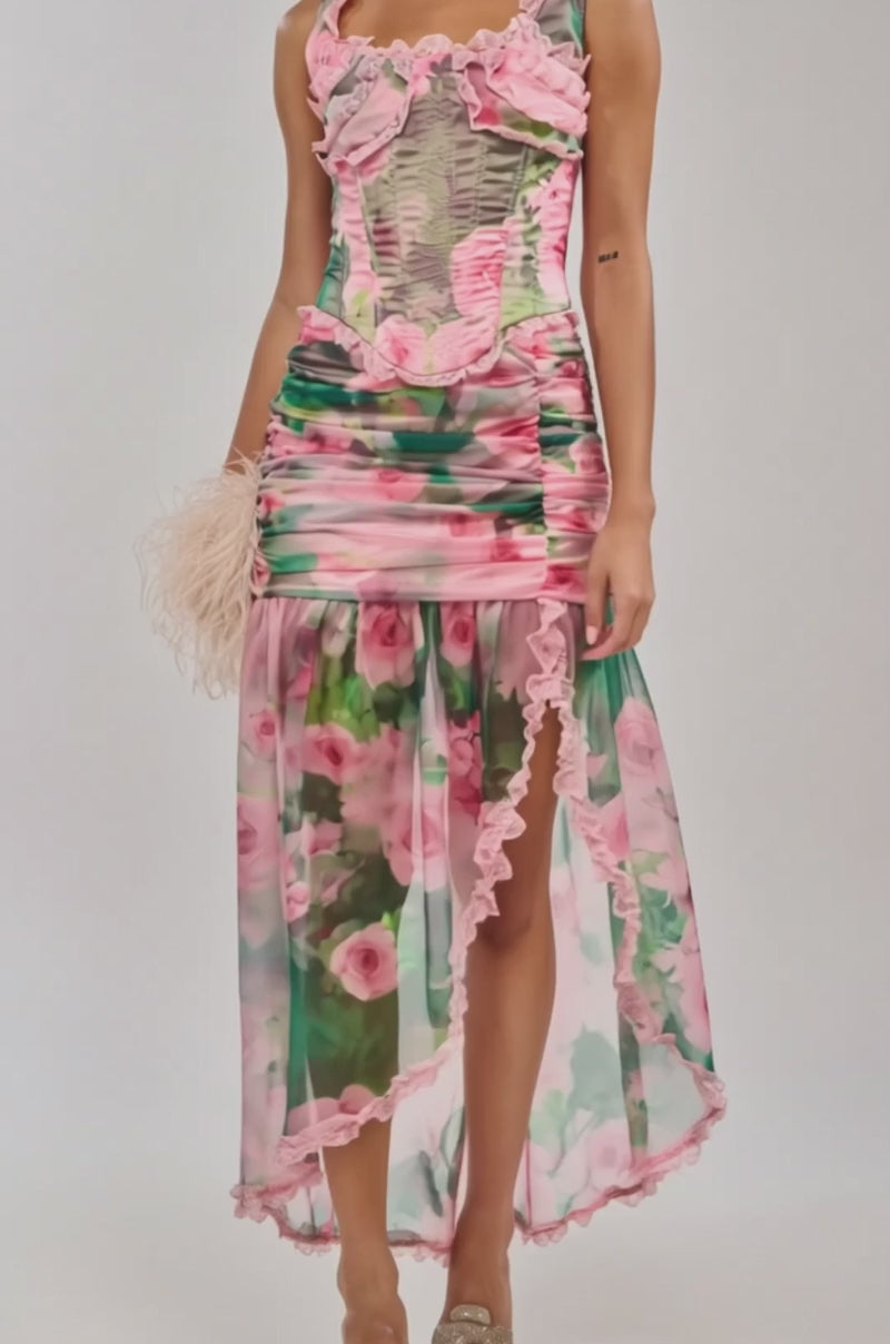 Video of woman modeling the DREAMING FLORAL CORSET dress with pink and green floral prints and lace details, holding a light pink feathered clutch. She stands before a plain light background, looking confidently at the camera.
