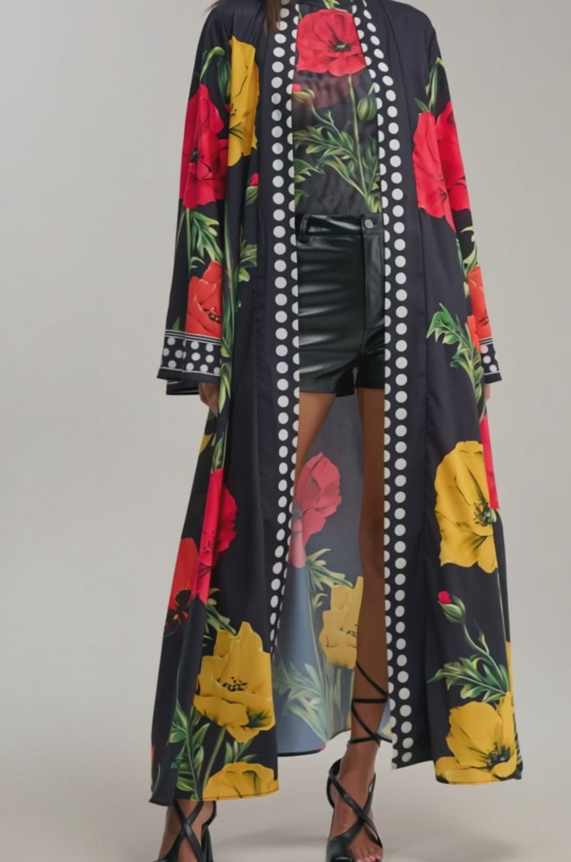 A video of a woman in the BELLADONNA SATIN DUSTER, featuring bold red and yellow florals with white polka-dot borders, styled with a floral top, black high-waisted shorts, and strappy heels.