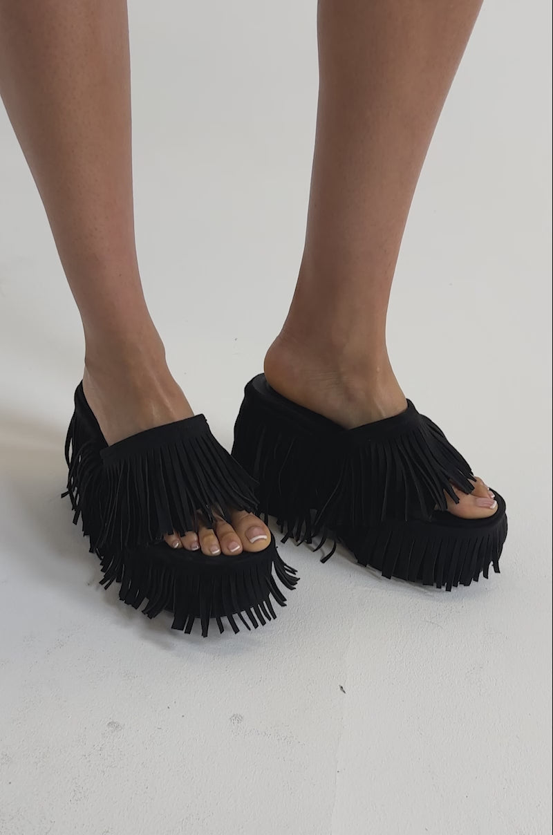 A video of a person wearing zebra print shorts and the AKIRA GOLD RAMYA BLACK FRINGE PLATFORM SANDAL, standing against a plain background. 