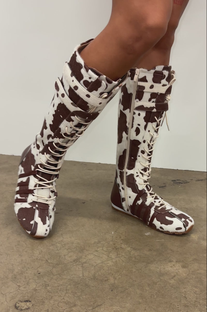 A video of a person wearing AZALEA WANG OZZY BROWN MULTI FLAT KNEE HIGH SNEAKER boots while standing indoors on a concrete floor.