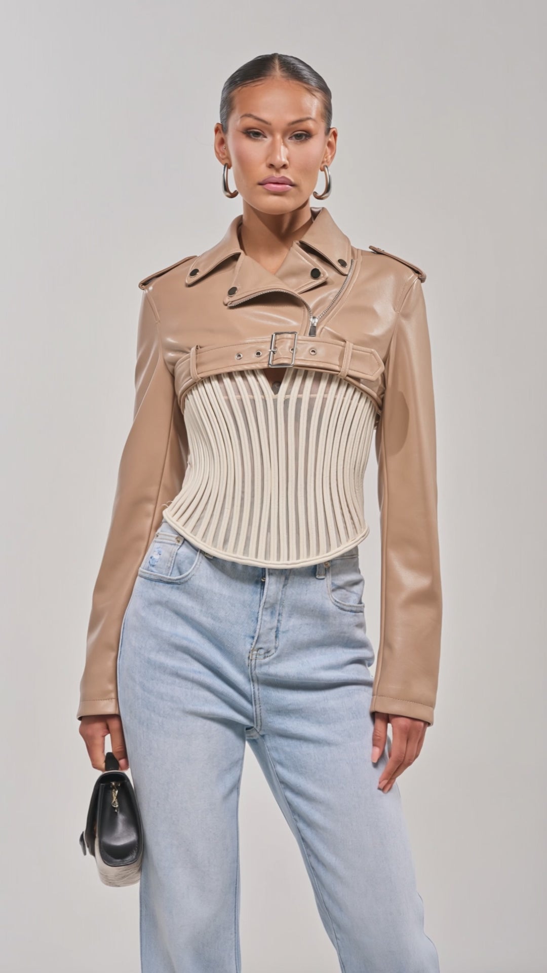 Video of woman modeling the HARLEY LUXE ULTRA CROP MOTO IN TAUPE over a white corset and light blue jeans, accessorized with a snakeskin clutch—an effortlessly chic look for a night out.
