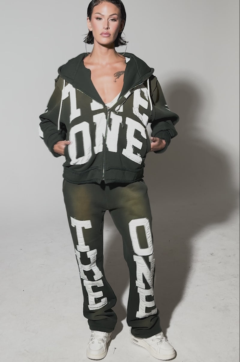 Video of woman modeling THE ONLY ONE JOGGER set with bold white lettering, wet-look hair, and white sneakers against a plain background.