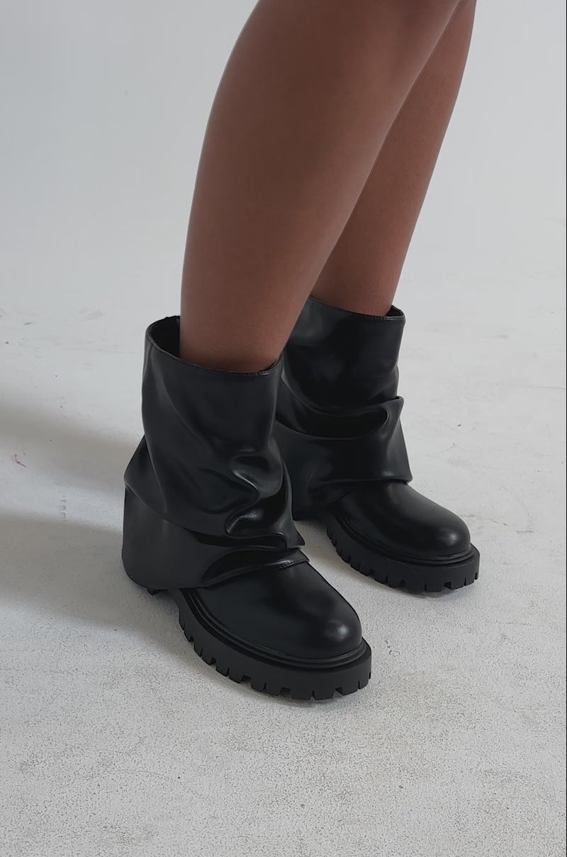 A video of a model wearing AZALEA WANG CLARKE BLACK PU SLOUCHY SHORT SHAFT COMBAT BOOTIES with chunky lug soles.