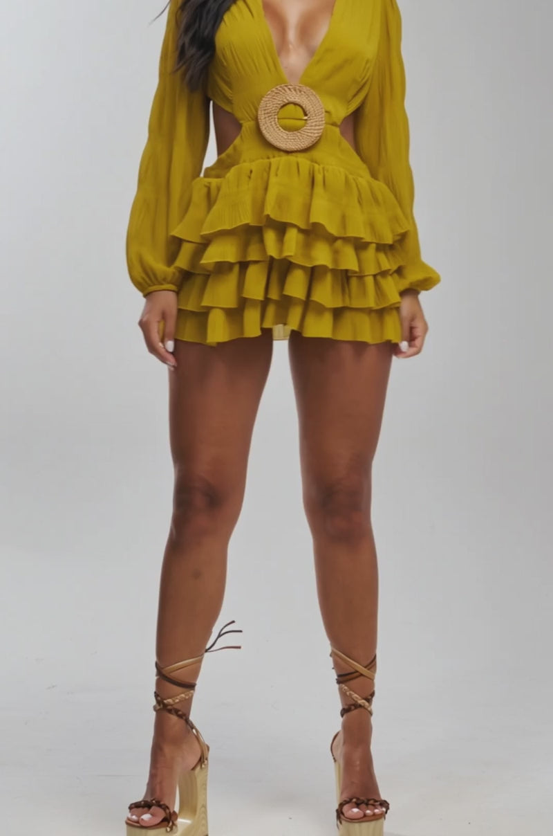Video of woman modeling the ON ISLAND TIME RUFFLED MINI DRESS IN CHARTREUSE, featuring ruffled long sleeves, a deep V-neck, circular belt at the waist, side cutouts, and a layered ruffled skirt. She stands against a light background.