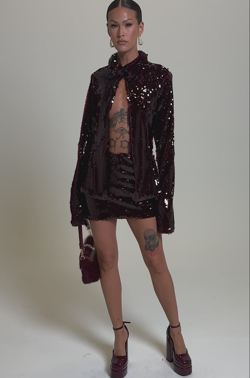 A video of a woman in the SHINING DOWN ON YOU SEQUIN MINI SKIRT and a matching burgundy blazer, revealing tattoos on her legs and torso. 