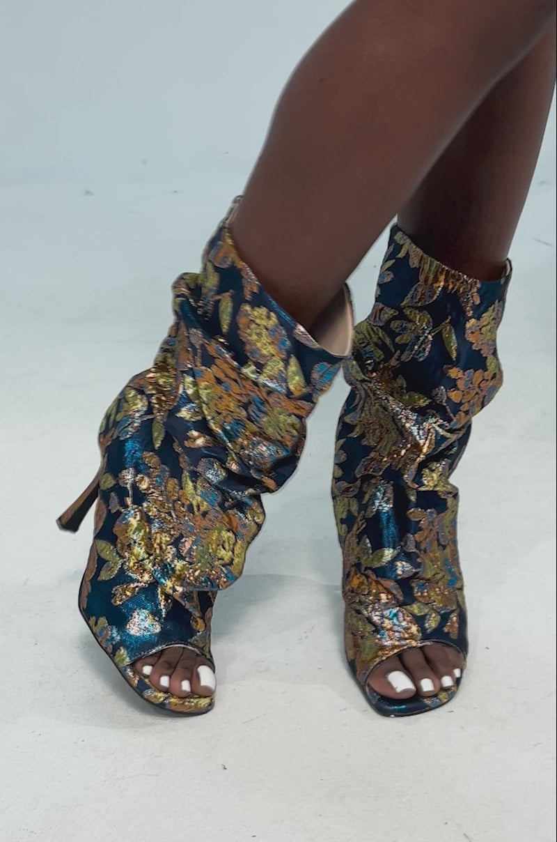 Video of woman modeling the AZALEA ROZSI BLUE MULTI BROCADE OPEN TOE STILETTO BOOTIE featuring a high heel, slouchy silhouette, and rich blue fabric with intricate gold and bronze florals for a striking metallic brocade effect.