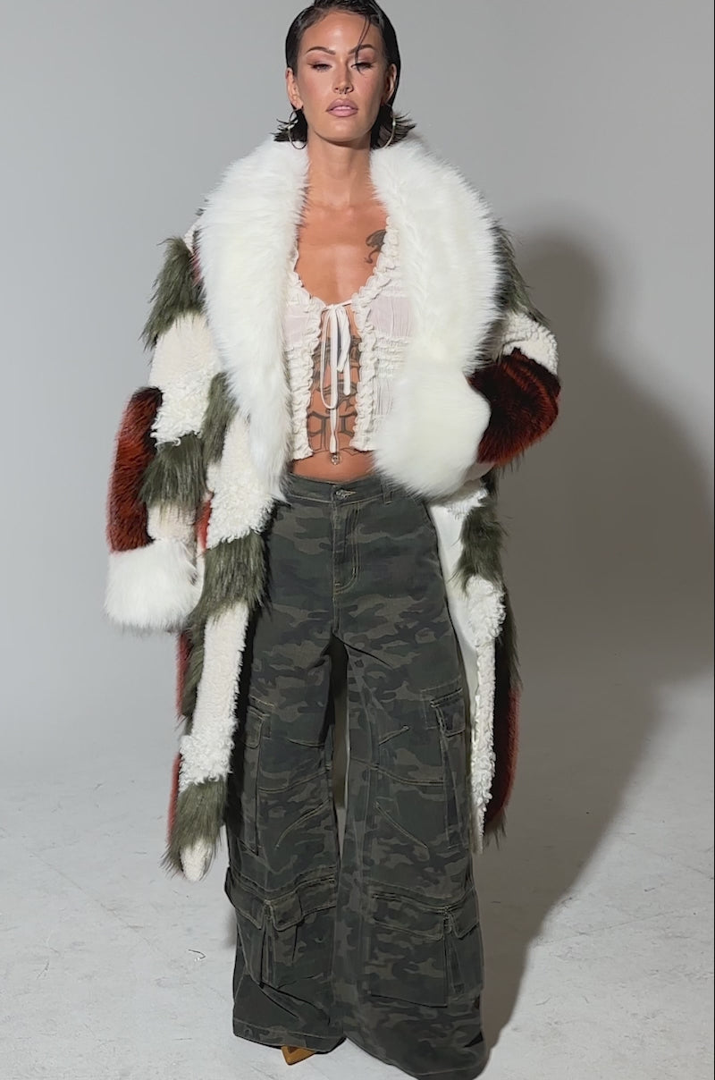 Video of woman modeling the FLEUR PATCHWORK FAUX FUR coat with white, olive, and rust panels over a ruffled white crop top and wide-leg camo pants, set against a plain light background.