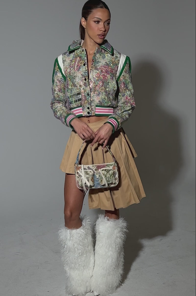 Video of woman modeling the TAPPED OUT RHINESTONE BOMBER with striped cuffs and faux leather trim, paired with a beige pleated skirt.