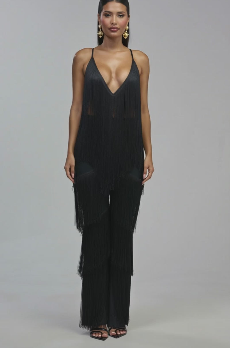 Video of a woman modeling the BAECATION FRINGE JUMPSUIT IN BLACK, which features long fringe accents, a deep V-neckline, and wide-leg pants. 