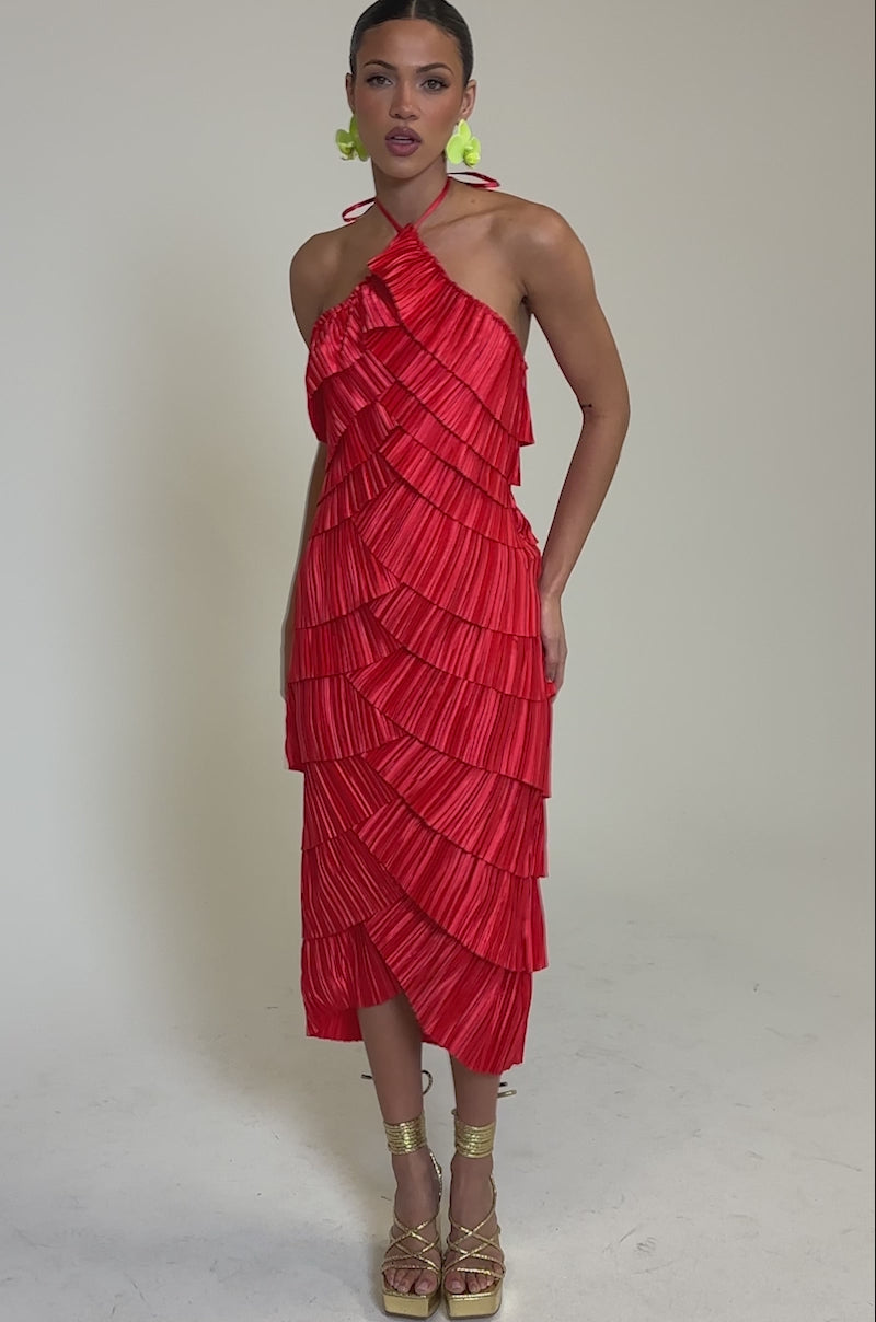 Video of woman modeling the GIVE IT TO ME BABY SATIN MAXI DRESS—a bright red, halter-neck, layered silhouette with accordion pleats and scalloped satin. Her hair’s pulled back, complemented by green earrings and strappy beige platform sandals.
