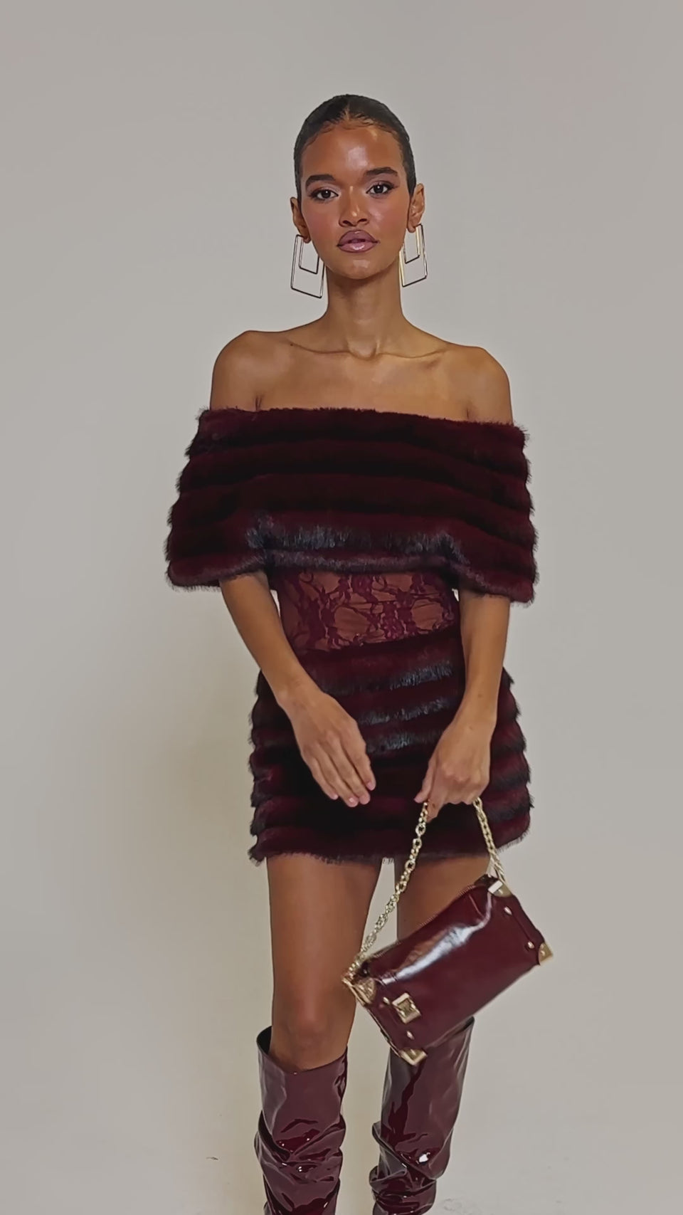 Video of woman modeling the SOFT CHERRY SLEEVELESS MINI DRESS with faux-fur panels and sheer lace waist detail, styled with geometric gold earrings, posing against a plain light background.