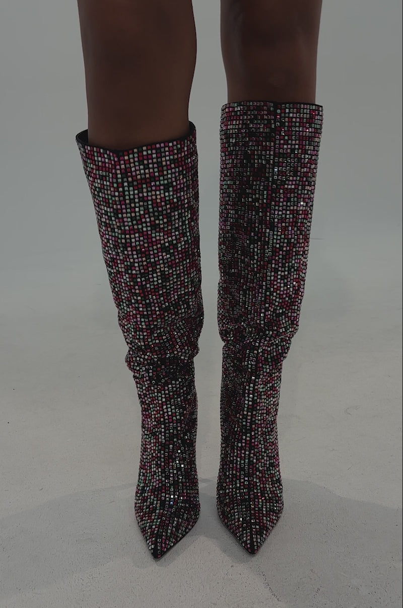 A video of a person in a burgundy blazer and the AZALEA WANG IZZY EMBELLISHED BOOT IN MULTI with stiletto heels stands in a spotlight against a neutral background.