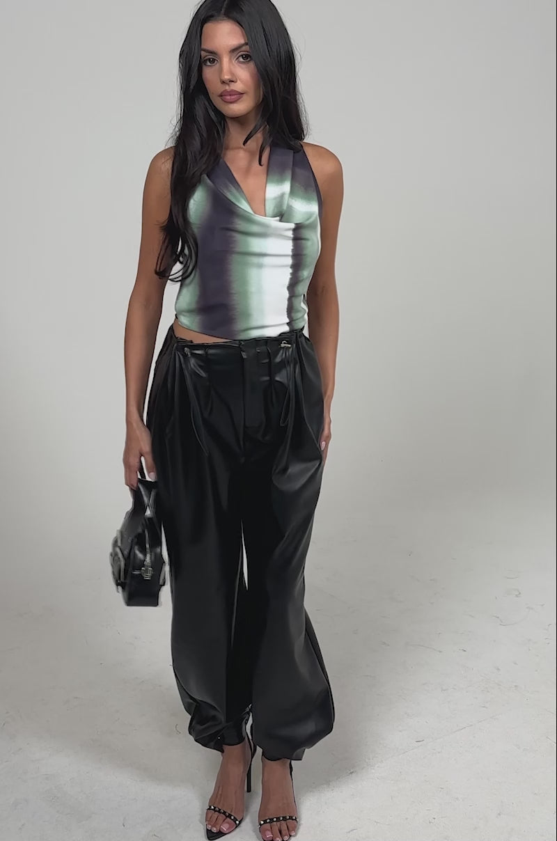 Video of woman modeling the ON TOP OF IT FAUX LEATHER TROUSER in black, holding a small black handbag and wearing black high-heeled sandals.