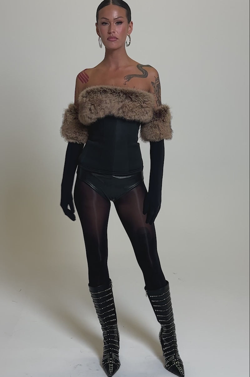 A video of a person in the SO CHIC Faux Leather Blouse with Fur Trim, paired with long black gloves, sheer tights, studded knee-high boots, large hoop earrings, and visible tattoos on one arm.