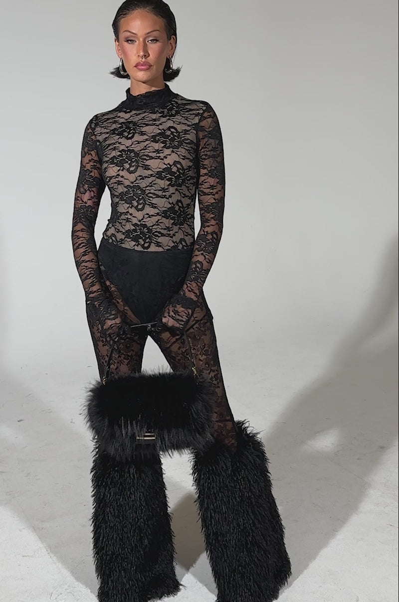 A video of a woman posing against a plain background wearing the ALL THE ATTENTION LACE GLOVE BODYSUIT, paired with black underwear, long lace gloves, black furry leg warmers, and holding a large black furry handbag while looking at the camera.