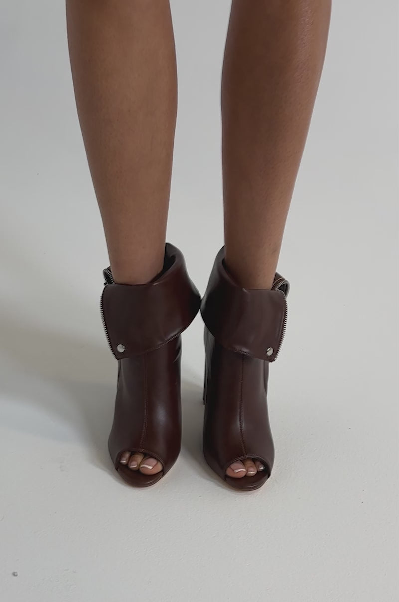 A video of a person wearing YANIX Brown PU Chunky Heel Booties with silver hardware, peep toe, folded cuffs, and side zippers against a neutral background.