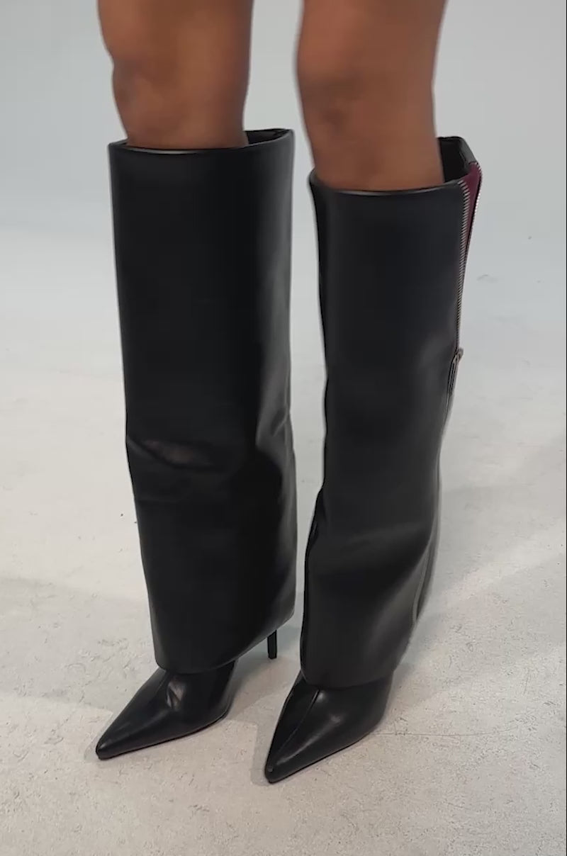 Video of woman modeling the AKIRA GOLD SHAQUILLE BLACK PU STILETTO BOOTS—shiny black faux leather, knee-high, pointed toes, stiletto heels, side zippers, and a hint of burgundy lining.