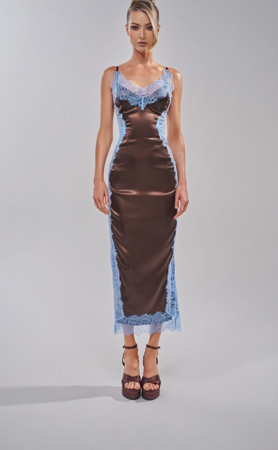 A video of a woman wearing the ESSENTIAL LACE TRIM SATIN SLEEVELESS MAXI DRESS IN BROWN with light blue lace trim. 