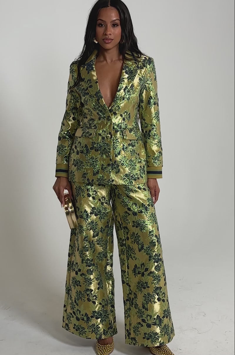 Video of woman modeling the HARLOW BROCADE WIDE LEG PANT and a gold floral blazer with a deep V-neck, styled with gold shoes and a matching clutch.
