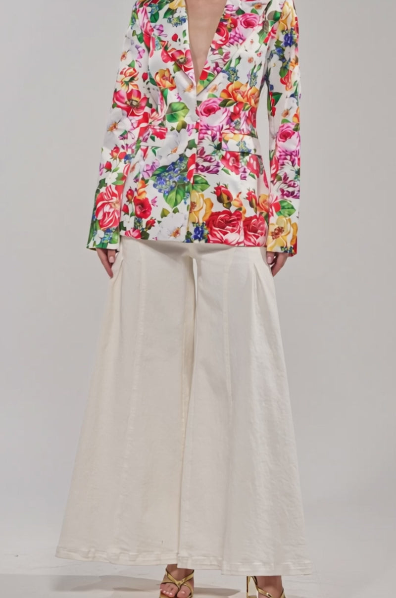 Video of woman modeling the ALESSANDRA SATIN BLAZER featuring a colorful floral pattern, deep neckline, and paired with light wide-leg pants.