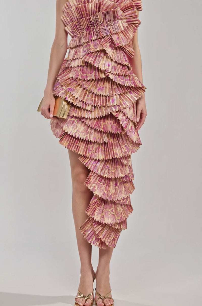 Video of woman modeling the LUST FOR LIFE ASYMMETRICAL BROCADE MINI DRESS, featuring sculptural layered ruffles in pink and gold. She accessorizes with gold earrings, a matching clutch, and strappy heels against a plain light background.