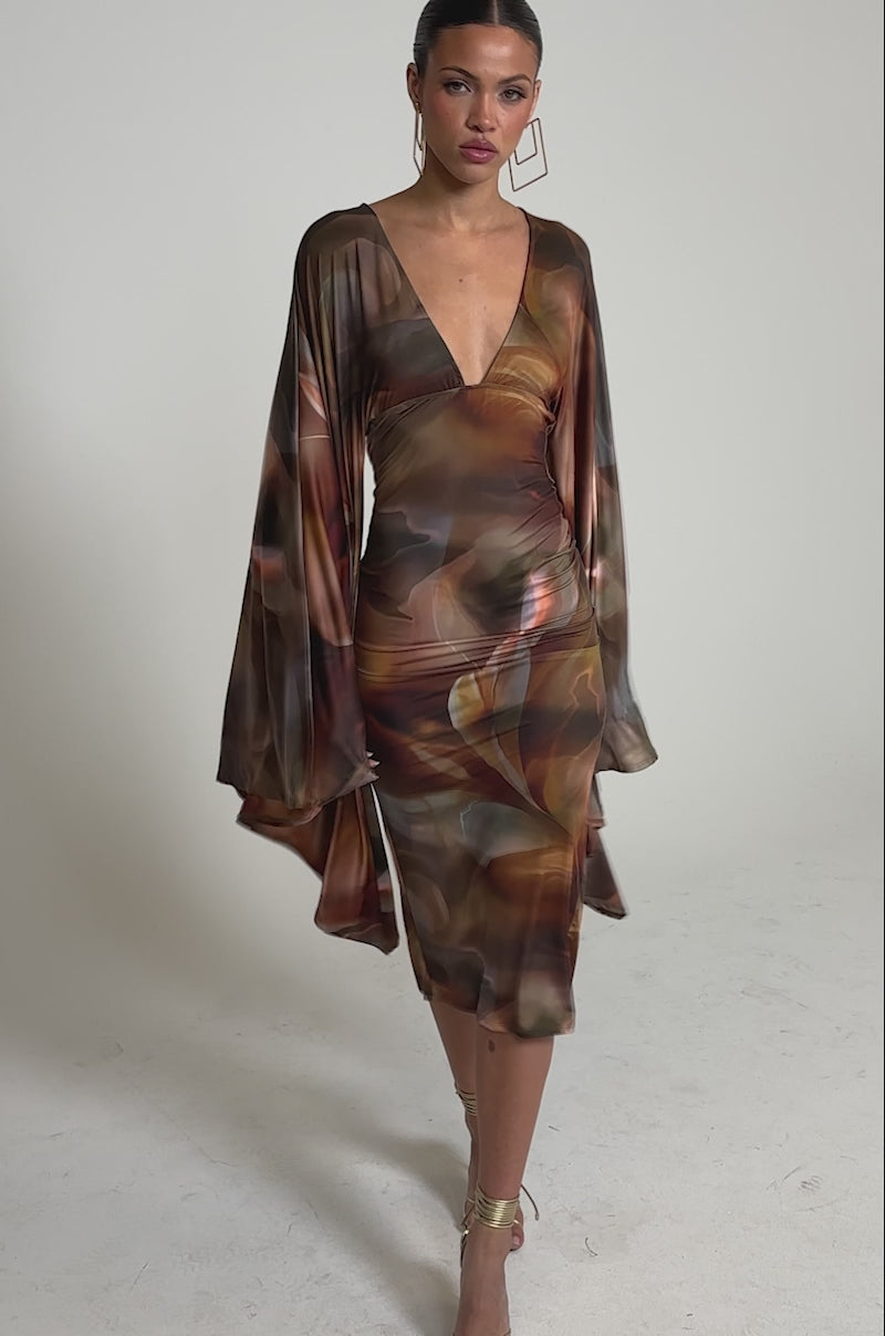 Video of woman modeling the SHINY LIKE ME MAXI DRESS with wide sleeves and a plunge neckline, paired with gold geometric earrings and strappy heels.