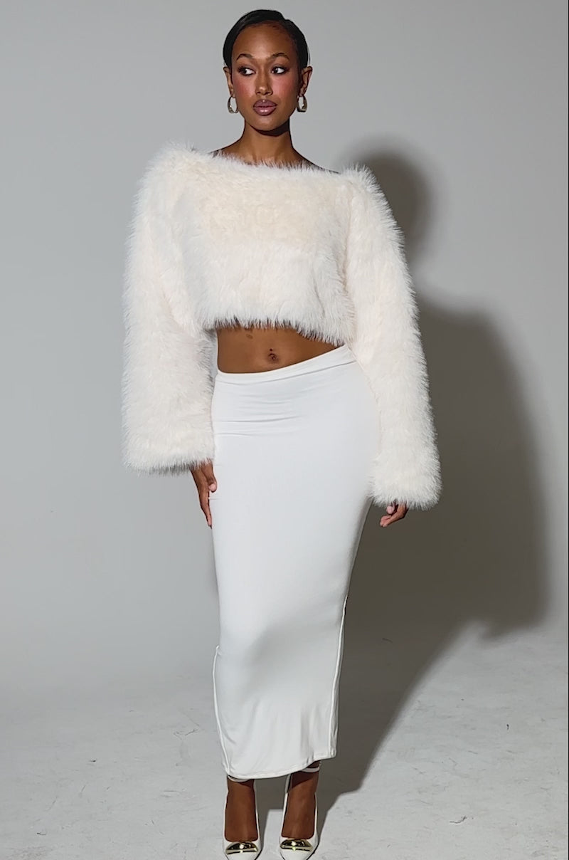 Video of woman modeling the COMFY COZY CROPPED SWEATER paired with a high-waisted white maxi skirt and gold pointed-toe heels against a plain light background.