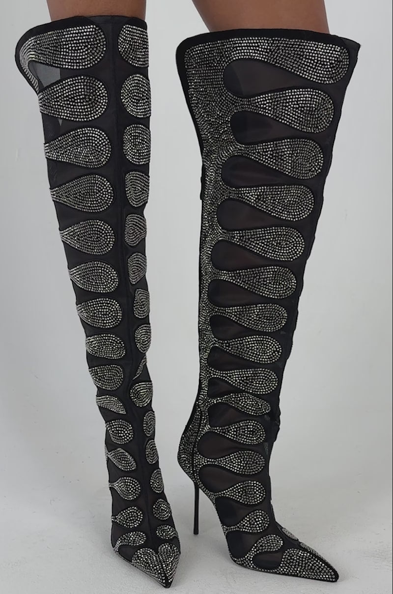 Video of a woman modeling the AKIRA GOLD AVENRA BLACK RHINESTONE THIGH HIGH STILETTO BOOT—featuring ornate cutout designs and sparkling embellishments.