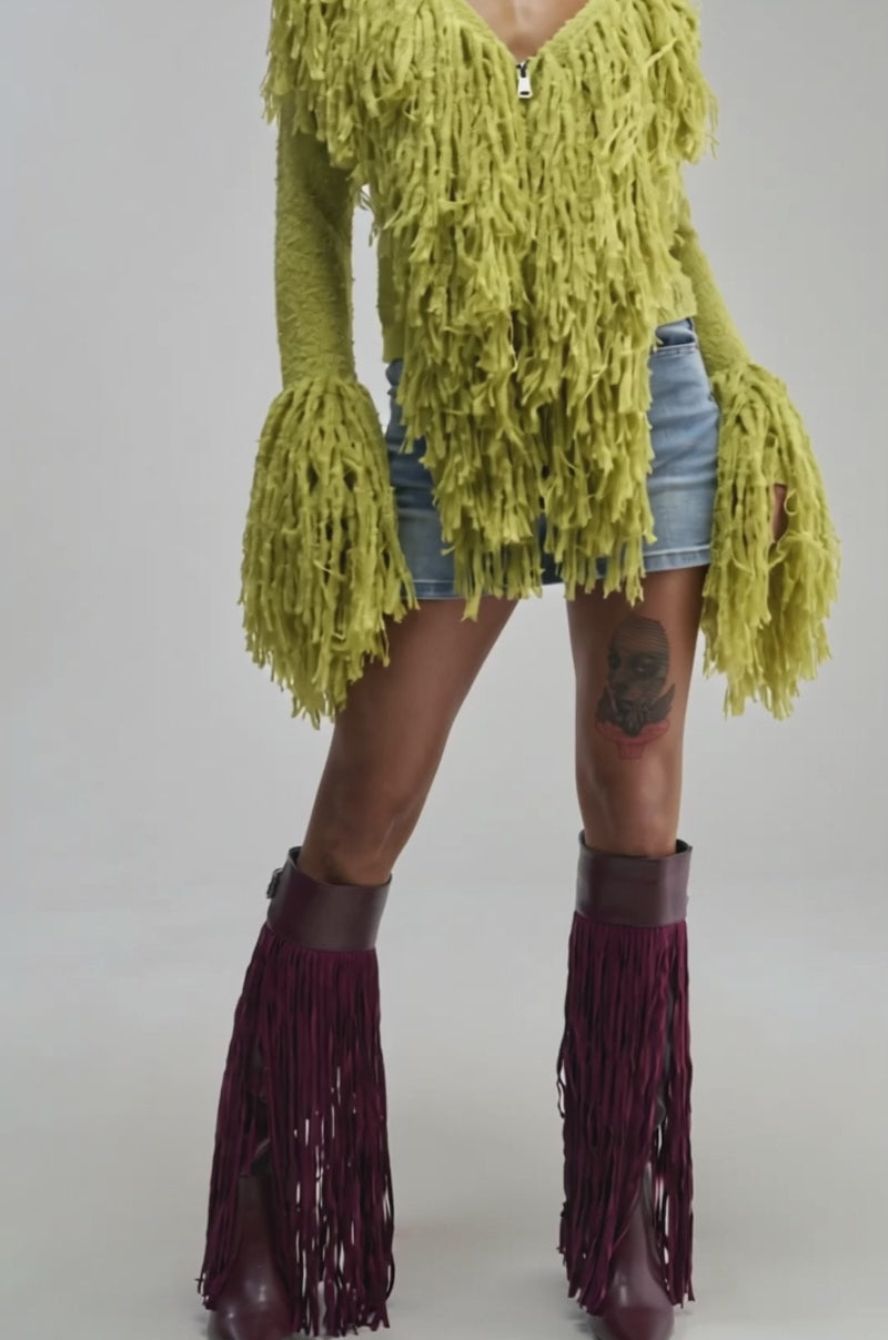 Video of a woman modeling the AT YOUR BEST FRINGE CARDIGAN IN CHARTREUSE with flared sleeves, styled as a standout statement piece and paired with a denim mini skirt.
