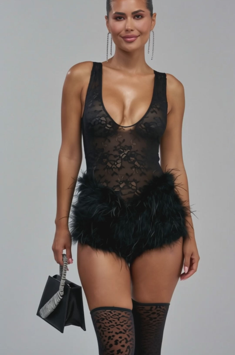 Video of a woman modeling the NECESSARY DRAMA FEATHER ROMPER—an alluring one-piece featuring black lace, a plunging neckline, and playful black feathered shorts.