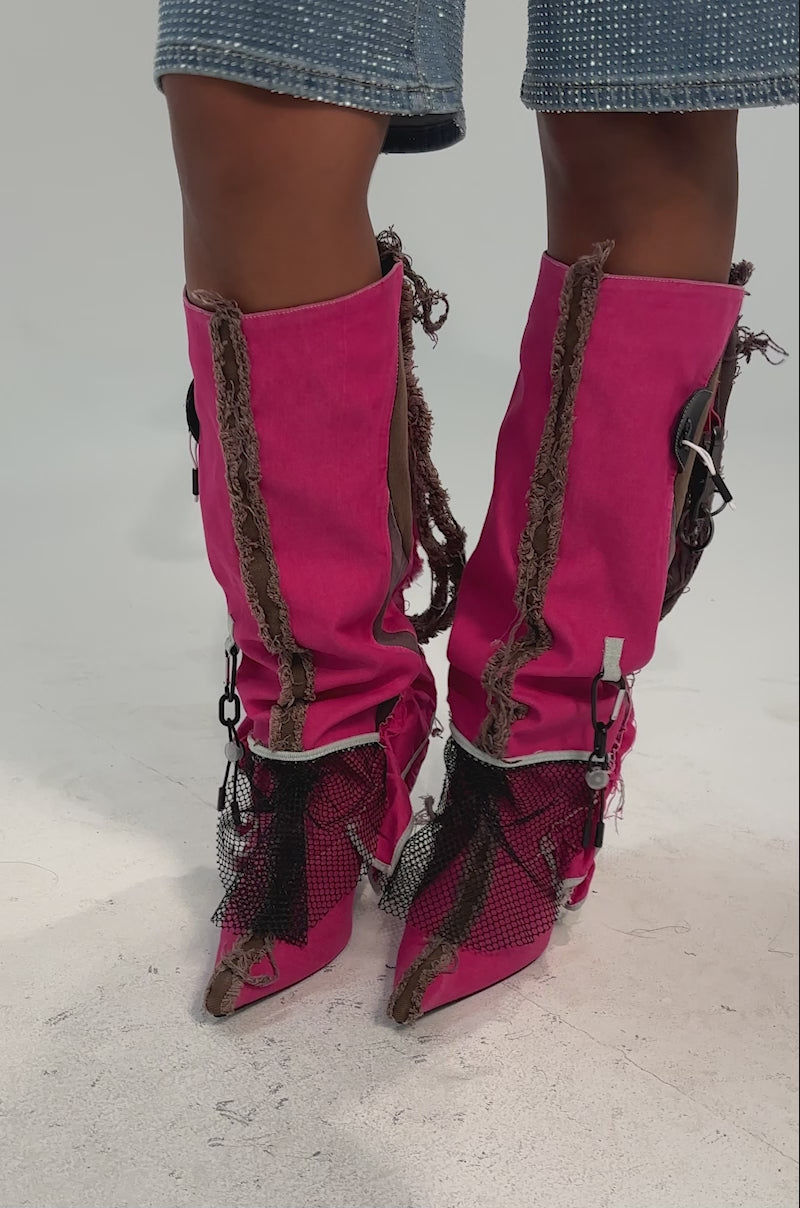 A video of a person wearing AKIRA GOLD COALESCE SPORTY MIXED MATERIAL STILETO BOOT with frayed fuchsia netting, decorative zippers, and brown patches, paired with knee-length light blue textured shorts. 
