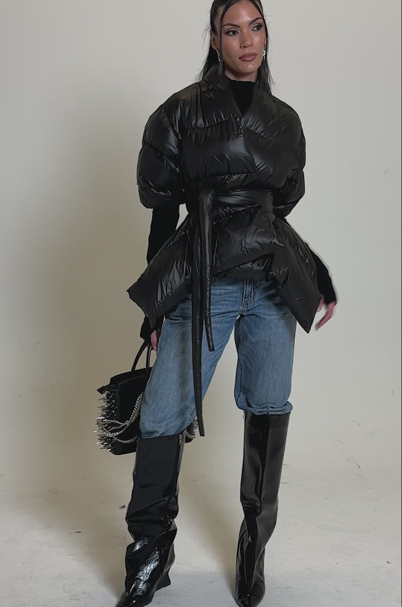 Video of woman modeling the A STEP AHEAD LONG RIBBED SLEEVE PEPLUM PUFFER COAT over a black top and blue jeans, holding a black handbag.