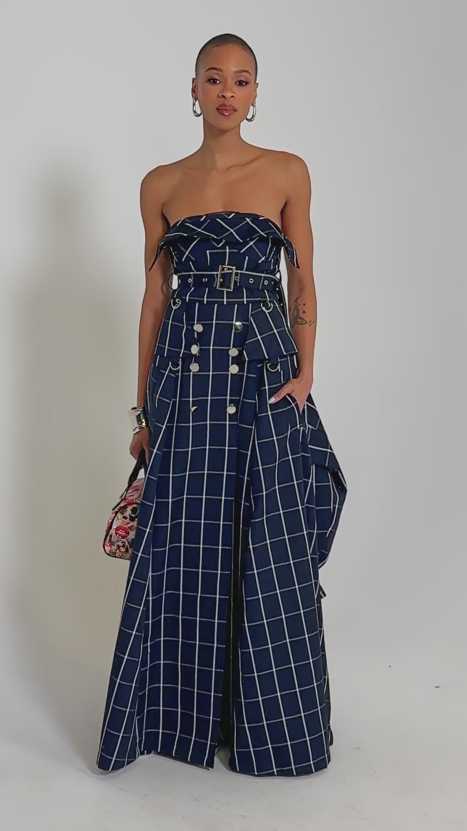 Video of woman modeling the DOWN TO BUSINESS PLAID MAXI DRESS with double-breasted buttons, a belt, high slit, mustard ankle boots, hoop earrings, a silver cuff, and carrying a floral handbag.