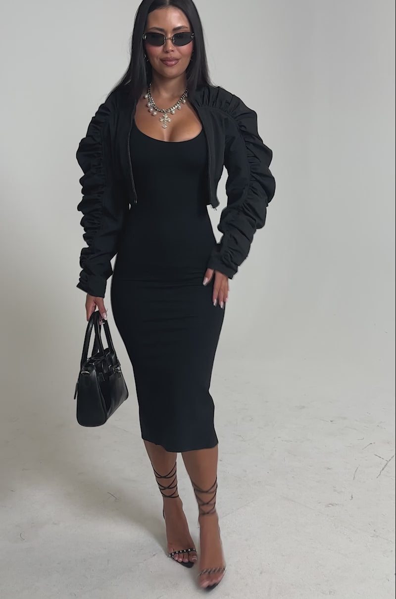 Video of woman modeling the NOTHING TO IT CROPPED BOMBER, a fitted black dress, layered silver necklaces, dark sunglasses, and holding a black handbag 