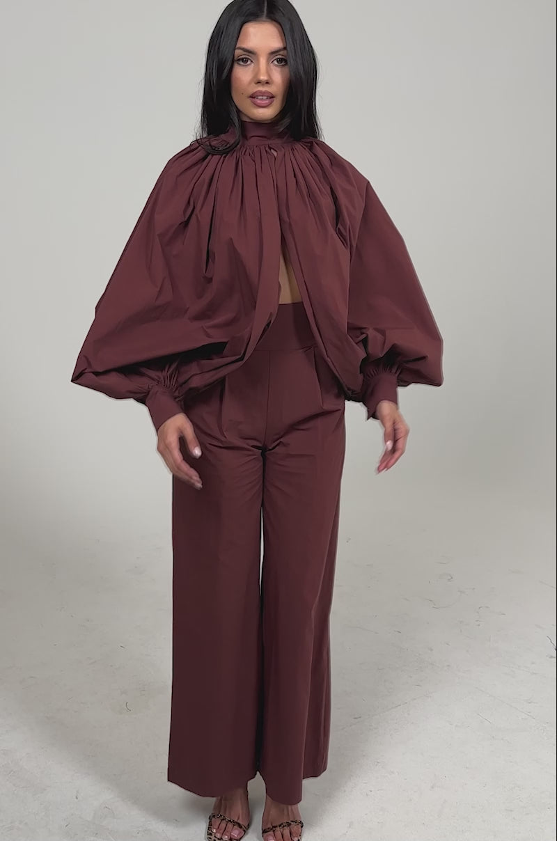 Video of woman modeling the GOLD COAST BALLOON SLEEVE BLOUSE IN BROWN with a high neck and front cutout, paired with matching high-waisted pants.