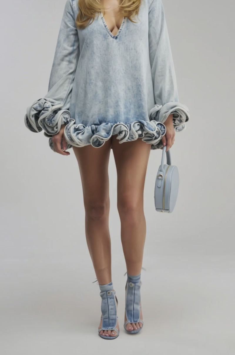 Video of a woman modeling the GIRLY GIRL MINI DRESS IN LIGHT BLUE DENIM, featuring long puffed sleeves and a ruffled hem.