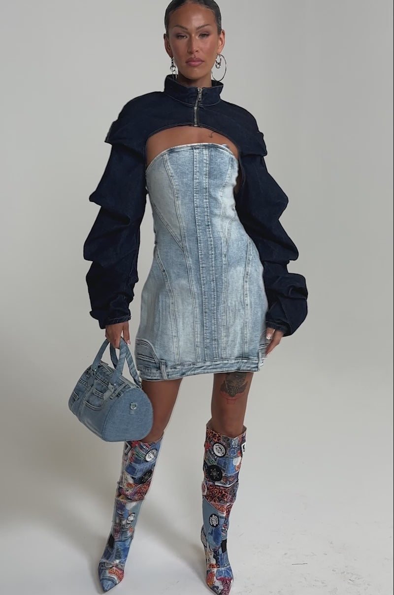 A video of a woman in the Spoil Me Bolero in Dark Denim, paired with a strapless mini dress, denim handbag, and tall patchwork boots. 