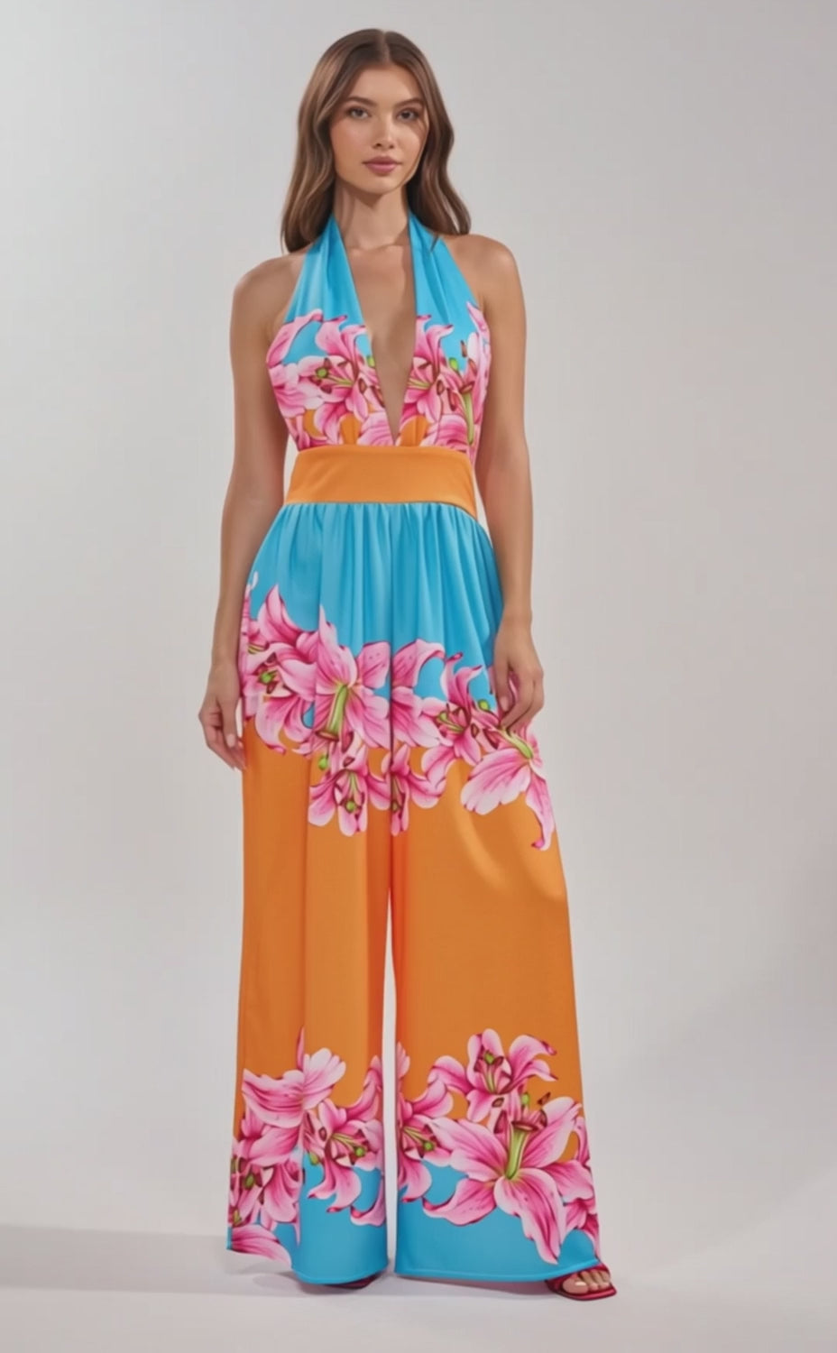 A video of a woman in the ON VACA TIME Halter Floral Print Maxi Dress, featuring vibrant blue and orange panels and tropical pink flowers.