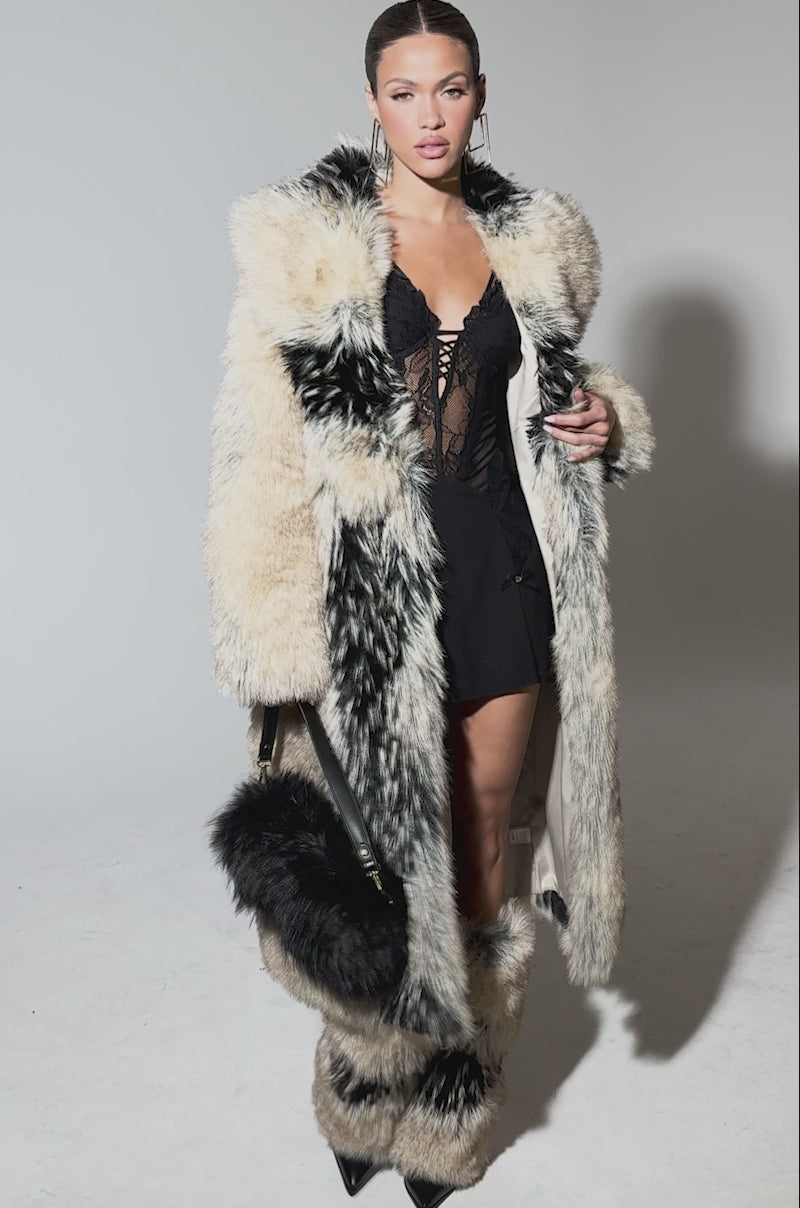 Video of woman modeling the TELLURIDE FAUX FUR IN TAN coat, paired with matching boots, a short black lace dress, and a black fur handbag.