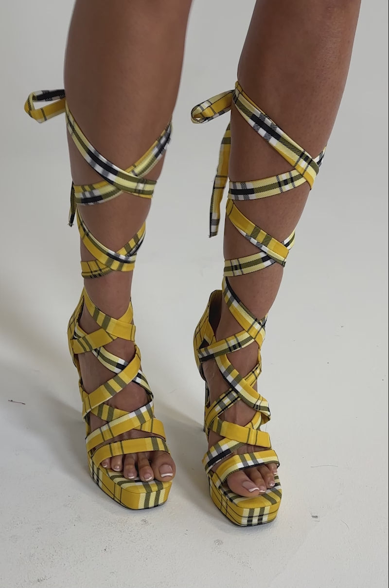 A video of a model wearing a short black skirt, a person stands on tiptoe in the AZALEA WANG JEMISHA YELLOW PLAID PLATFORM LACE UP SANDAL.