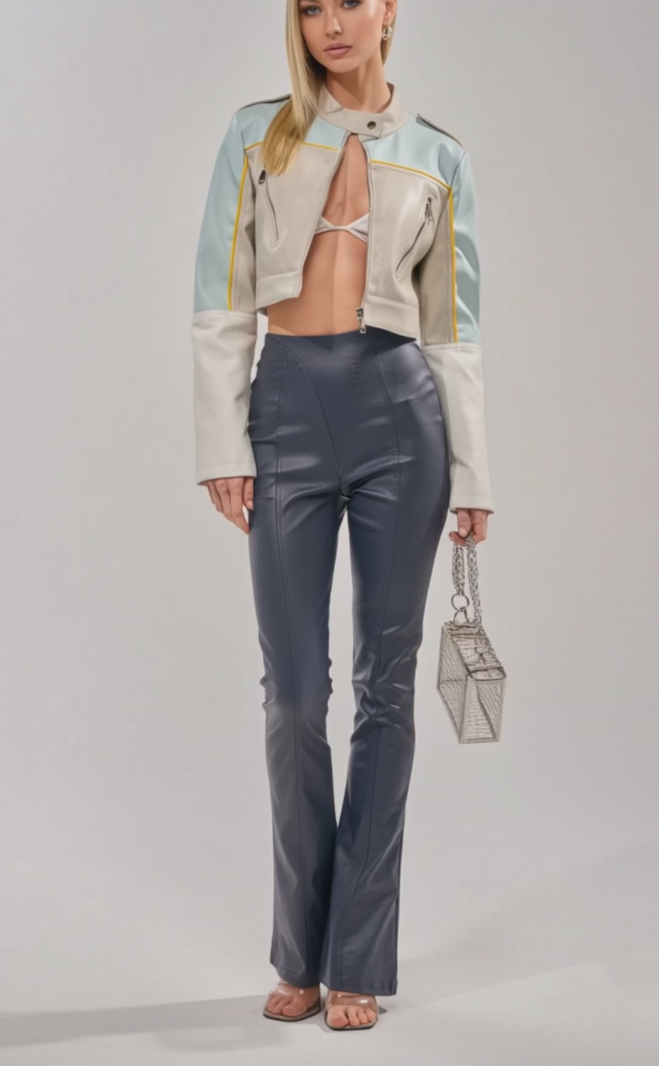 Video of woman modeling the BETTER LUCK CROPPED MOTO IN LIGHT BLUE jacket over a strappy bra top and shiny navy high-waisted pants, her straight blonde hair contrasting with the plain, light background.