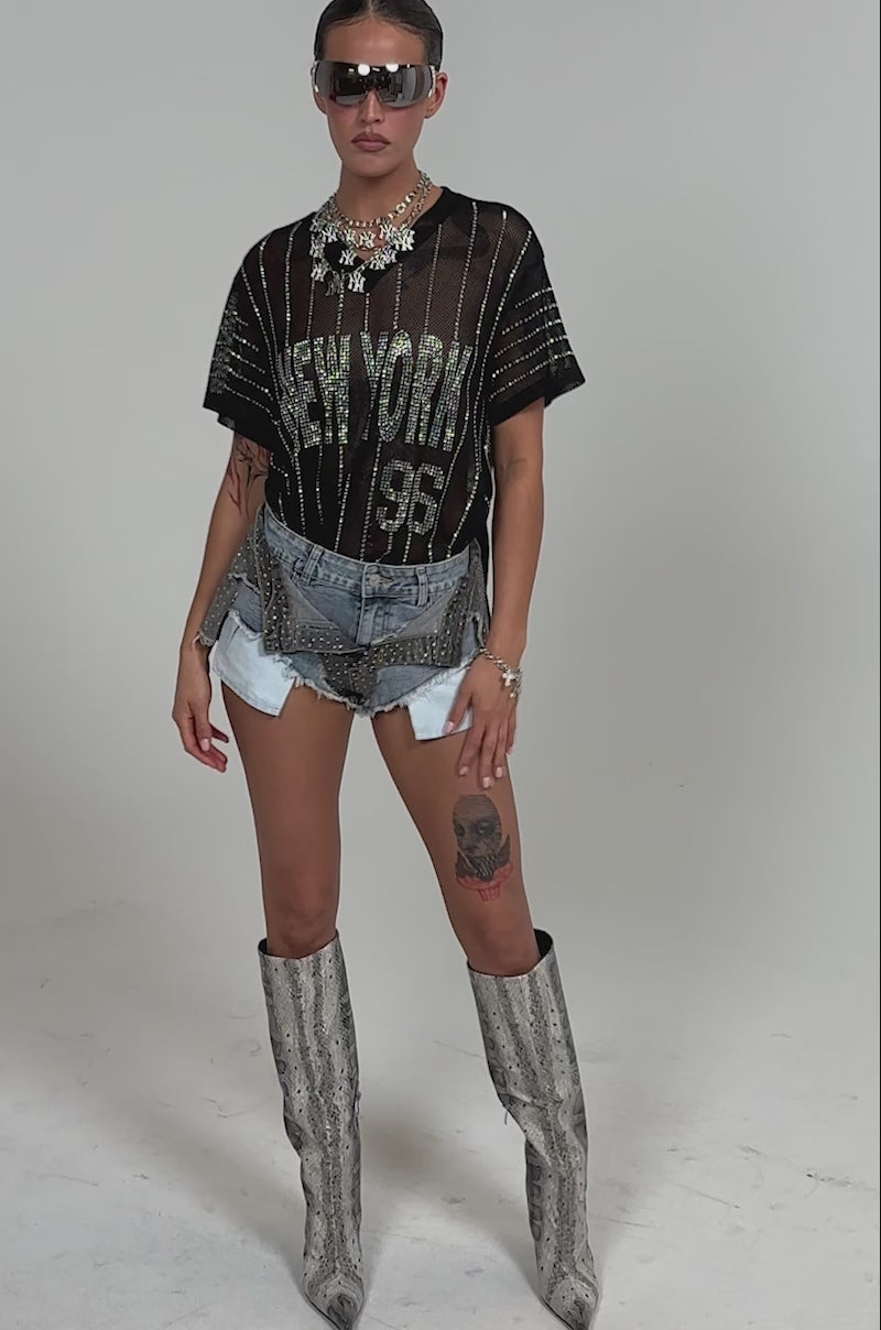 Video of woman modeling the HOTTY ALERT MICRO SHORT layered with a sheer black mesh top, and showing a thigh tattoo of a skull 