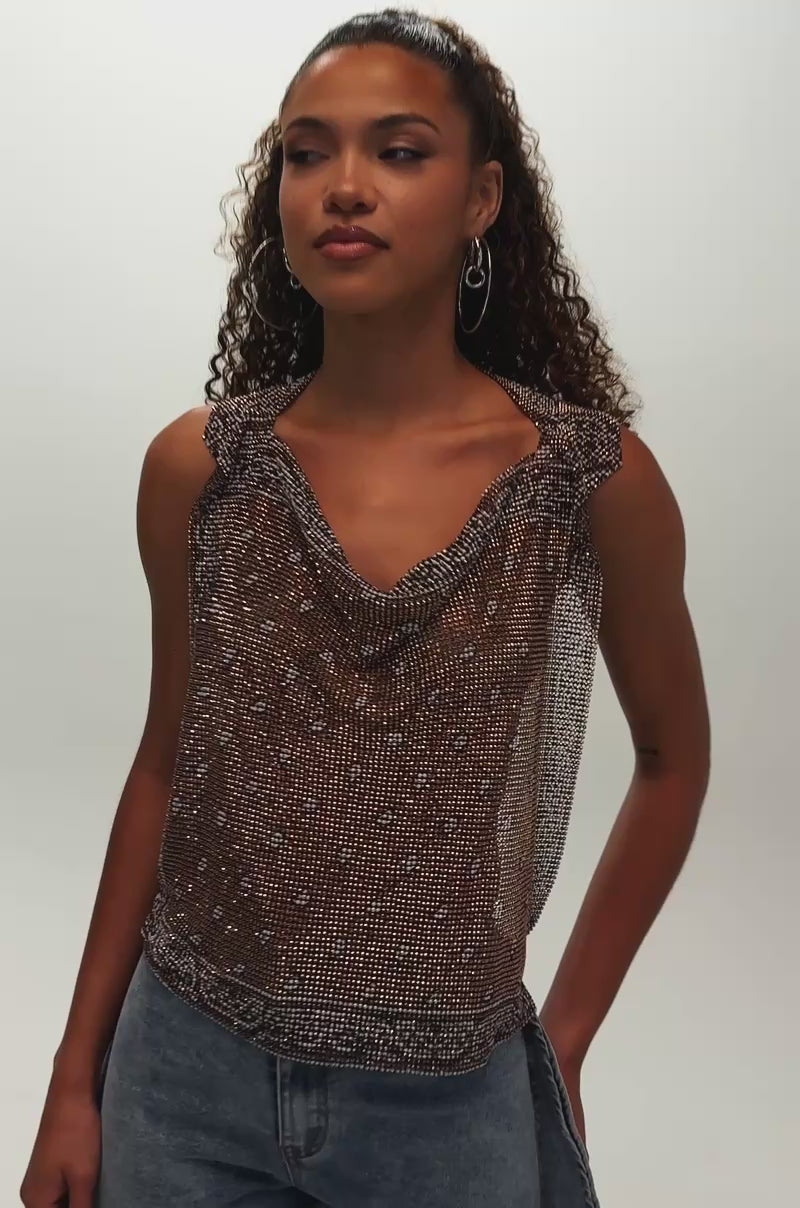 Video of woman modeling the BRONZE BANDANA PRINT RHINESTONE TOP, a brown, sleeveless western festival style with small white dots and ruffle details, paired with blue wide-leg jeans. She faces left with a neutral expression against a plain background.