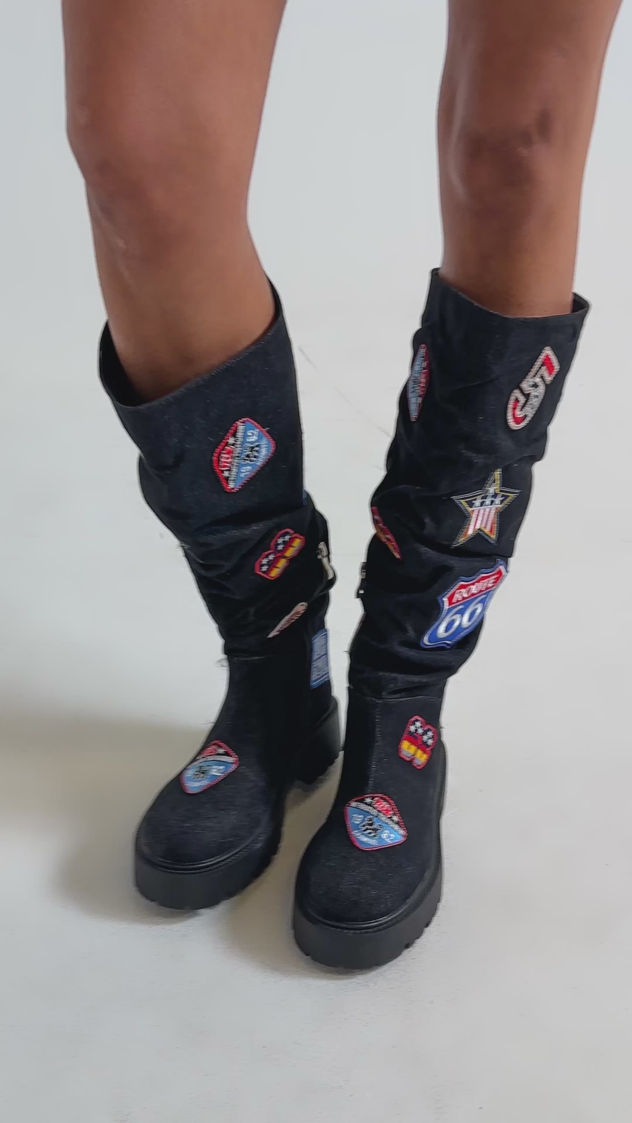 Video of woman modeling the AKIRA GOLD POSTAL BLACK PATCHWORK FLAT BOOT, featuring colorful route and highway patches