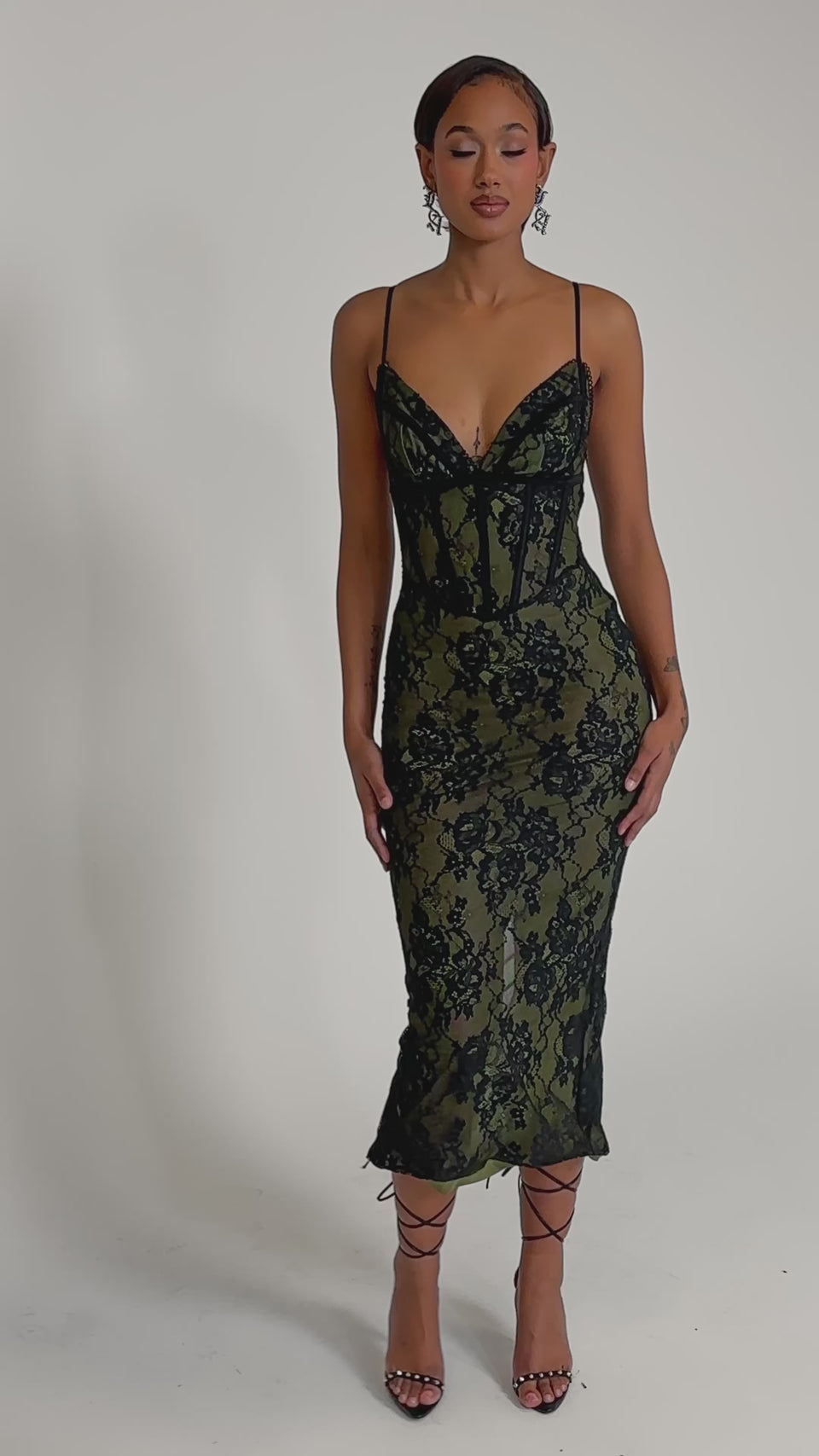 A video of a woman wearing the BETTER BELIEVE IT LACE MAXI DRESS—an olive green and black fitted maxi with lace details, spaghetti straps, and a sweetheart neckline. 
