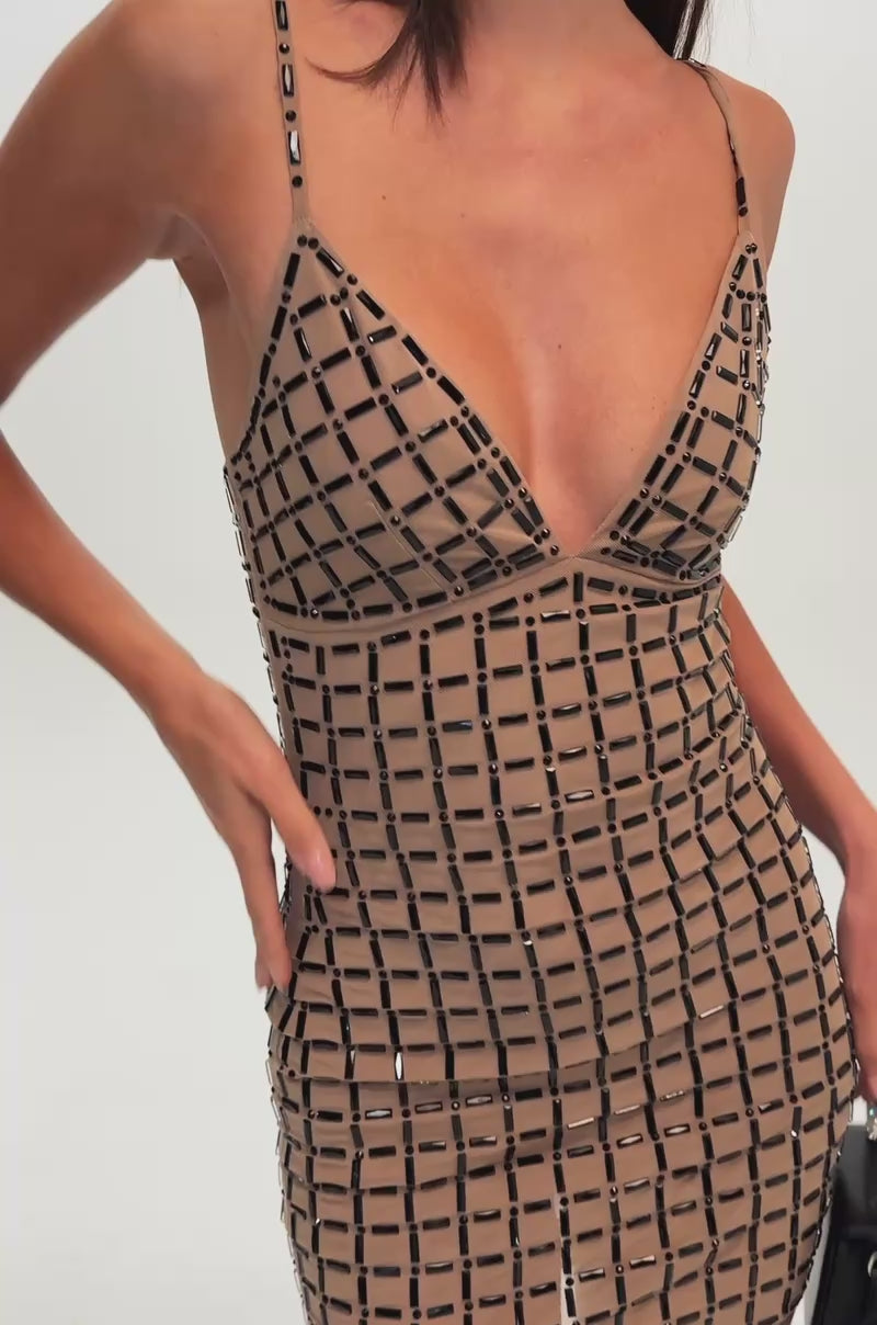 A video of a woman wearing the CITY LIGHTS RHINESTONE MINI DRESS—a fitted, sleeveless nude mini dress featuring a black geometric grid pattern. 