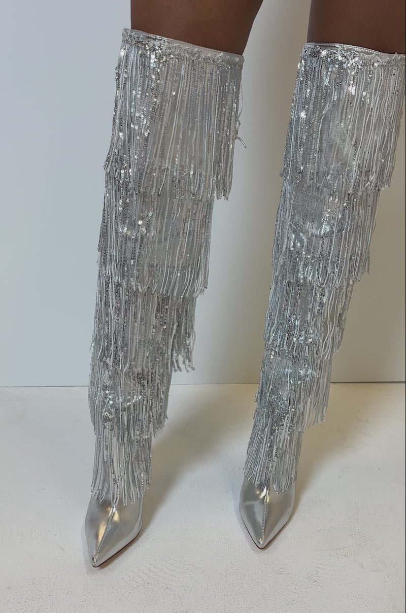Video of person modeling the AZALEA WANG ADRIEL SILVER FRINGE BOOT. It is a knee-high metallic boot adorned with layers of silver fringe 