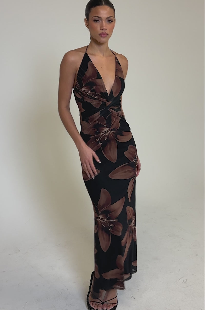 Video of woman modeling the FLOWER CHILD MAXI DRESS— a sleeveless, floor-length floral print with large blooms, halter neckline, and open-back detail—against a plain light background.
